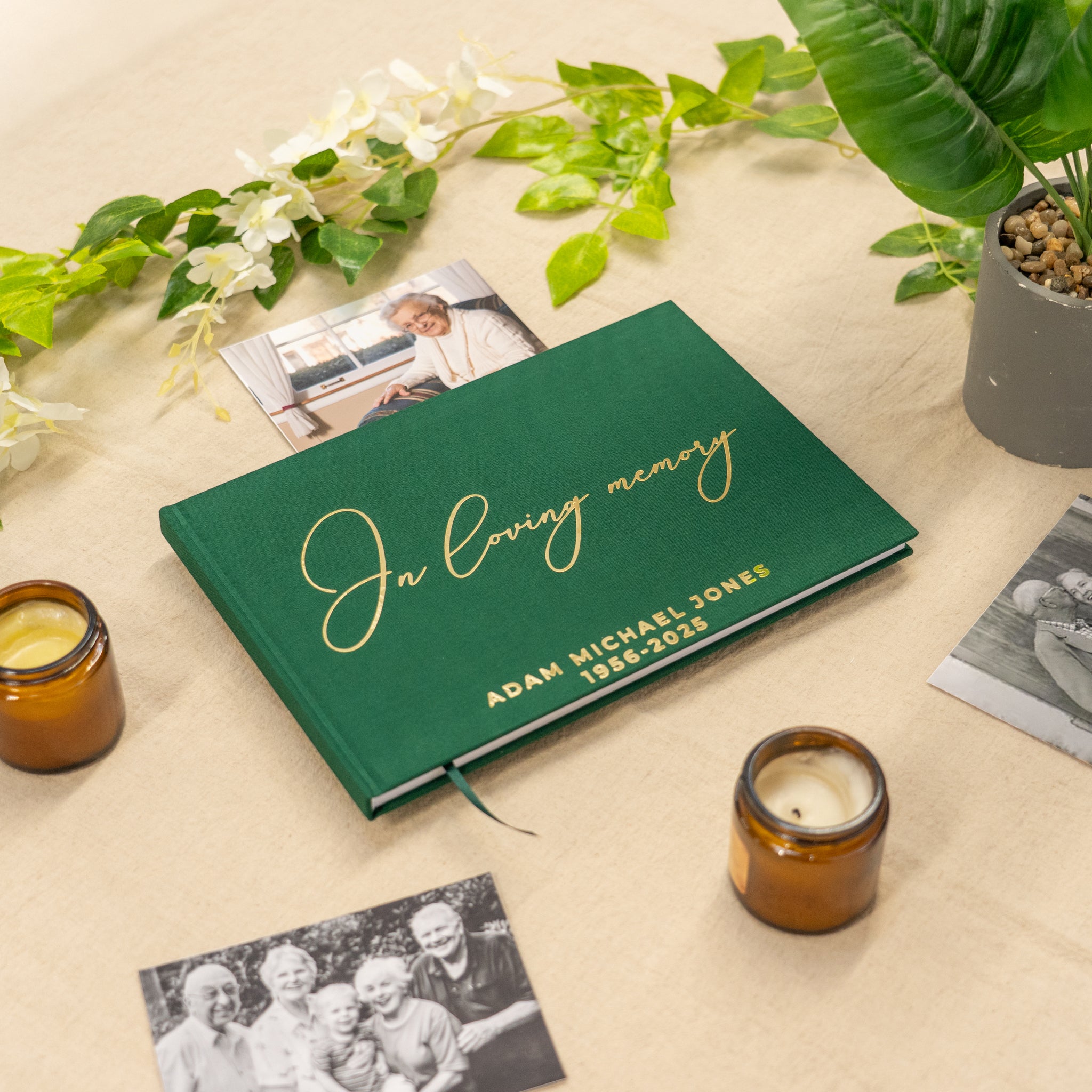 Green纪念册 with 'In loving memory' text on a beige surface with candles and photos.