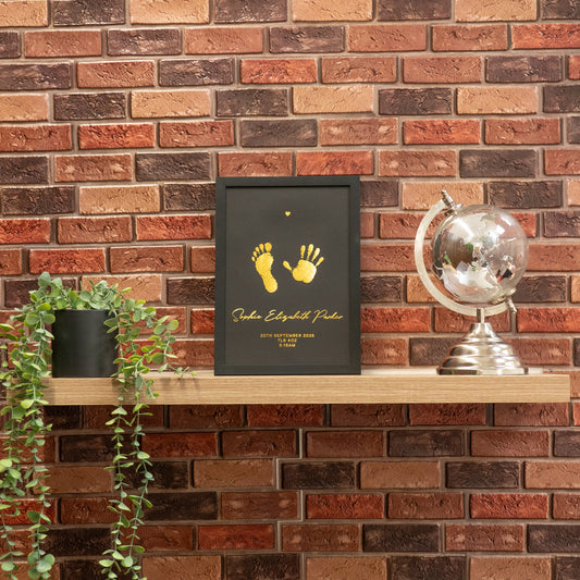 Framed artwork with footprints on a wooden shelf against a brick wall.