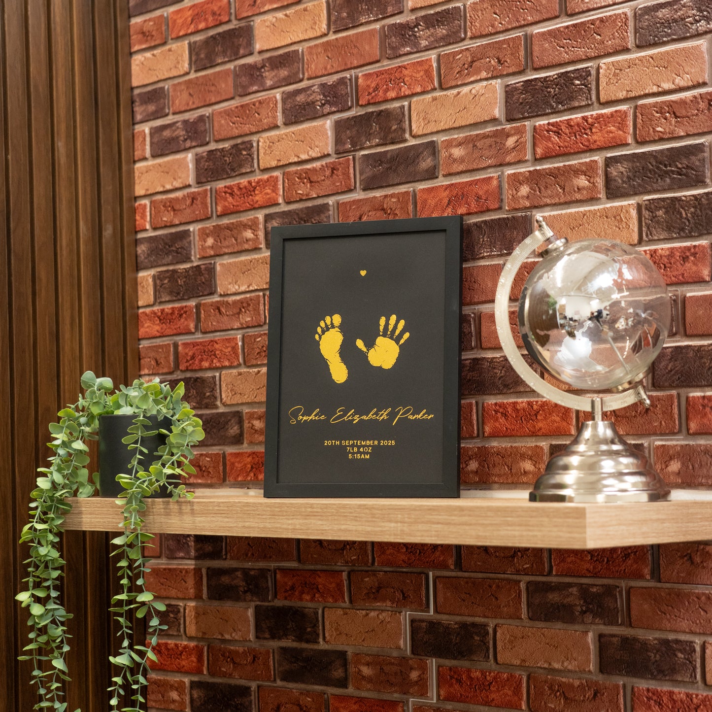 Framed artwork with yellow footprints and text on a wooden shelf against a brick wall.