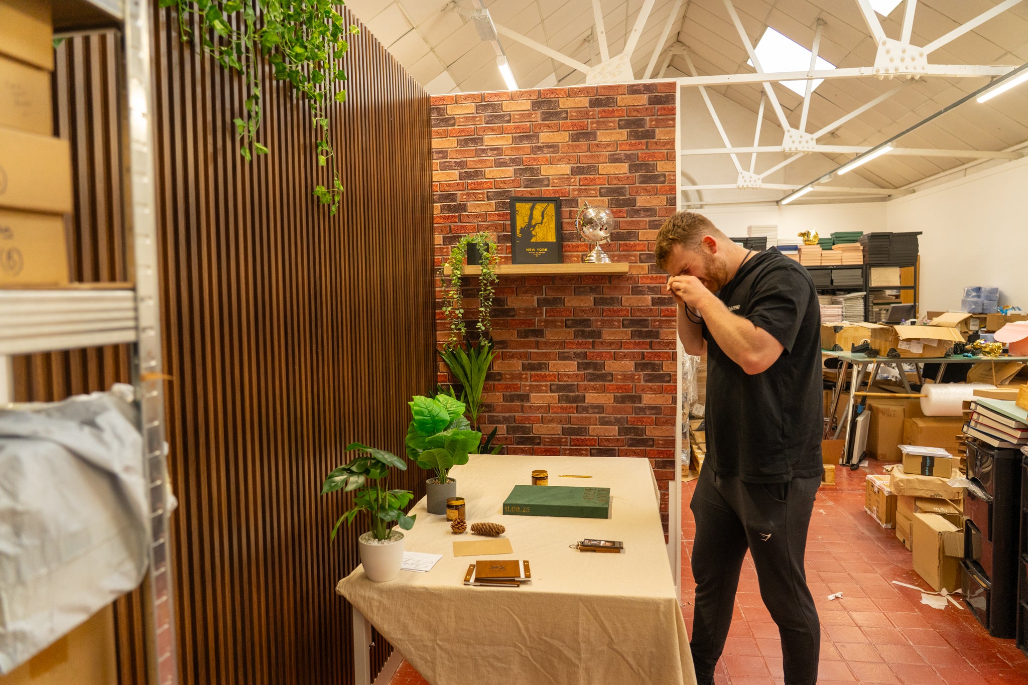 Person standing in a room with a table displaying plants and small items, surrounded by boxes and furniture.