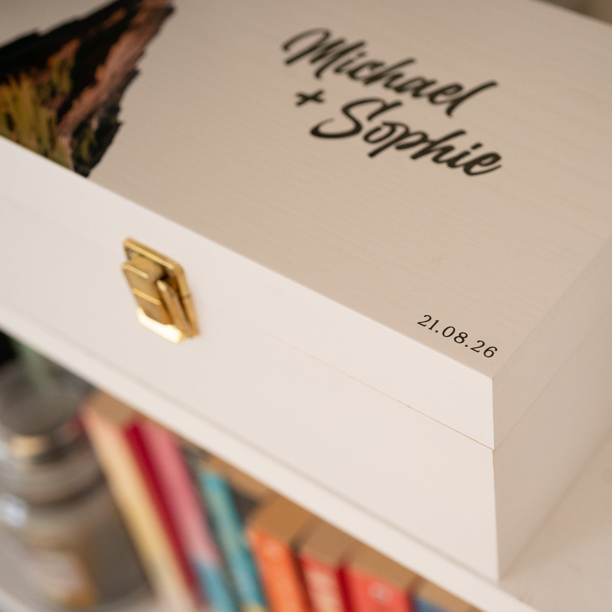 A close-up of a personalized white wooden keepsake box with a gold clasp, featuring the names 'Michael + Sophie' and the date '21.08.