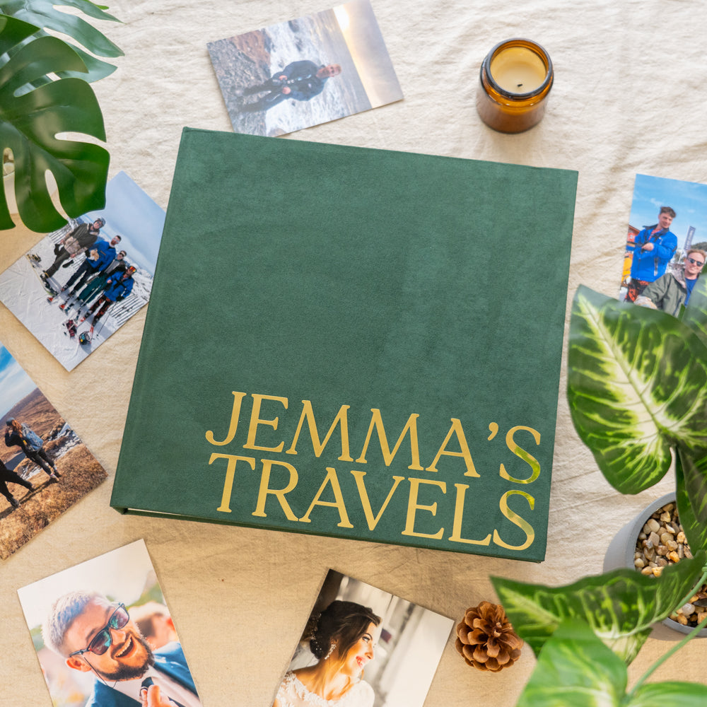 Green travel album titled 'Jemma's Travels' surrounded by travel photos on a wooden surface.