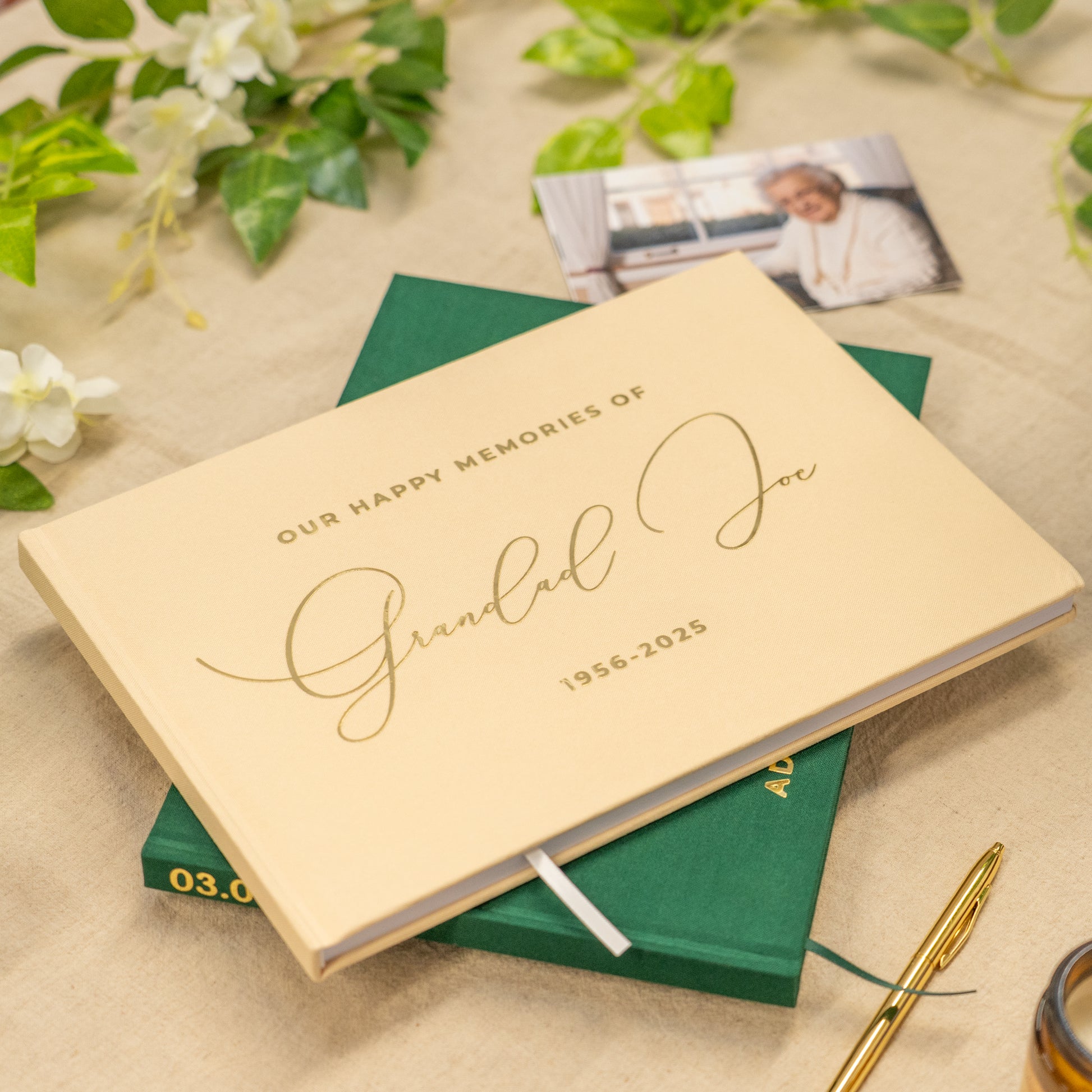 Personalized memory book titled 'Our Happy Memories of Grandad Joe' on a decorative surface with flowers and a pen.