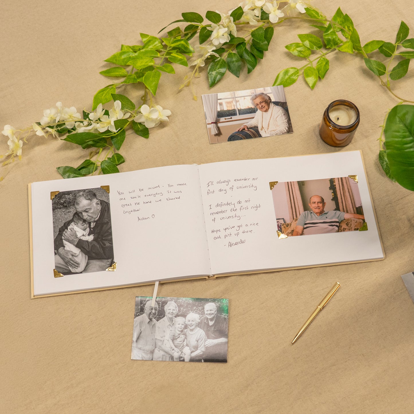 Open photo album with family photos on a beige surface with greenery and a candle.