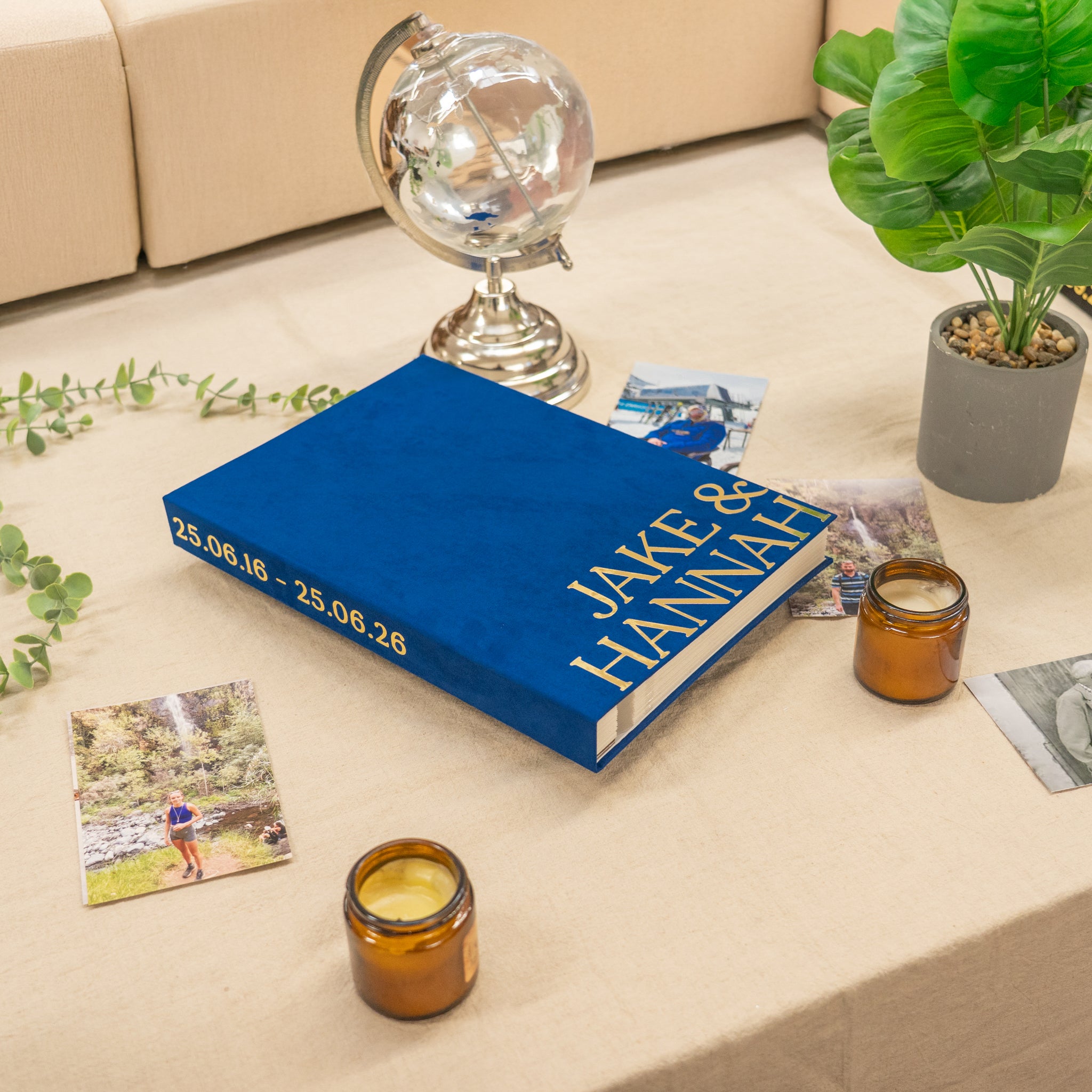 Blue book with gold text on a coffee table with candles, photos, and a plant.