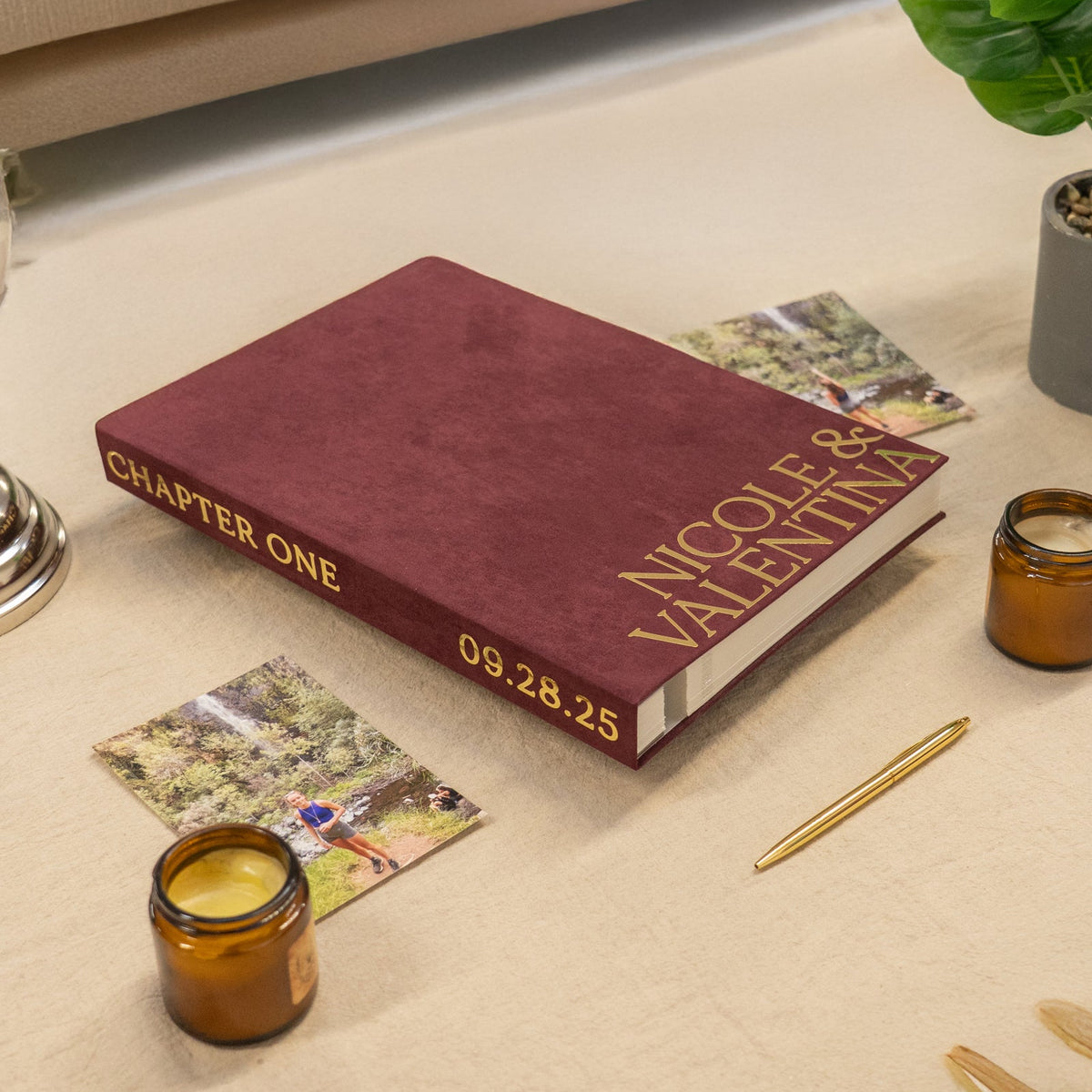 Maroon book titled 'Chapter One' with personalized text on a beige surface, surrounded by candles and a plant.