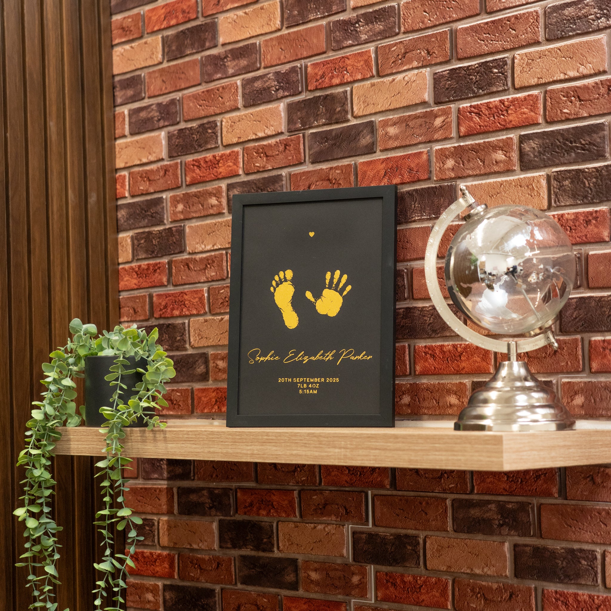 Framed artwork with yellow footprints and text on a wooden shelf against a brick wall.