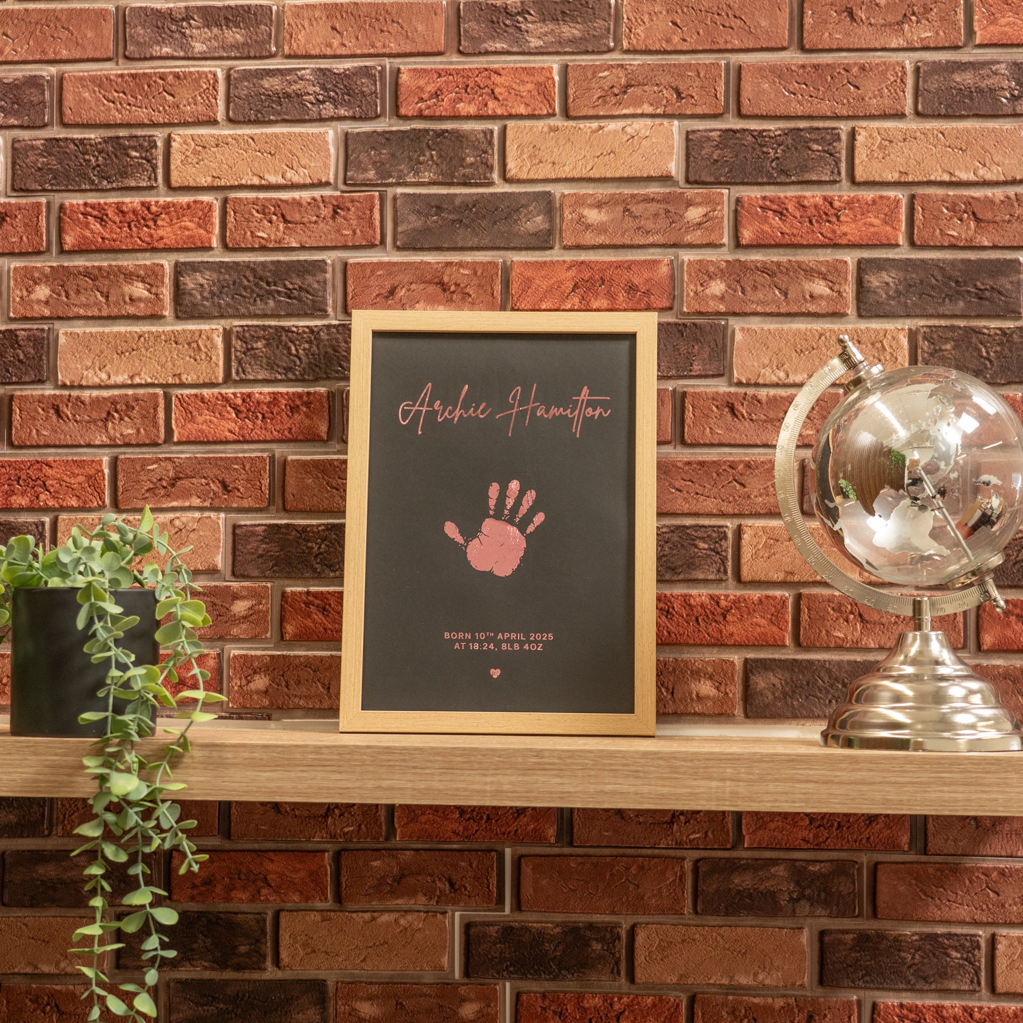 Framed artwork with handprint and text on a wooden shelf against a brick wall.