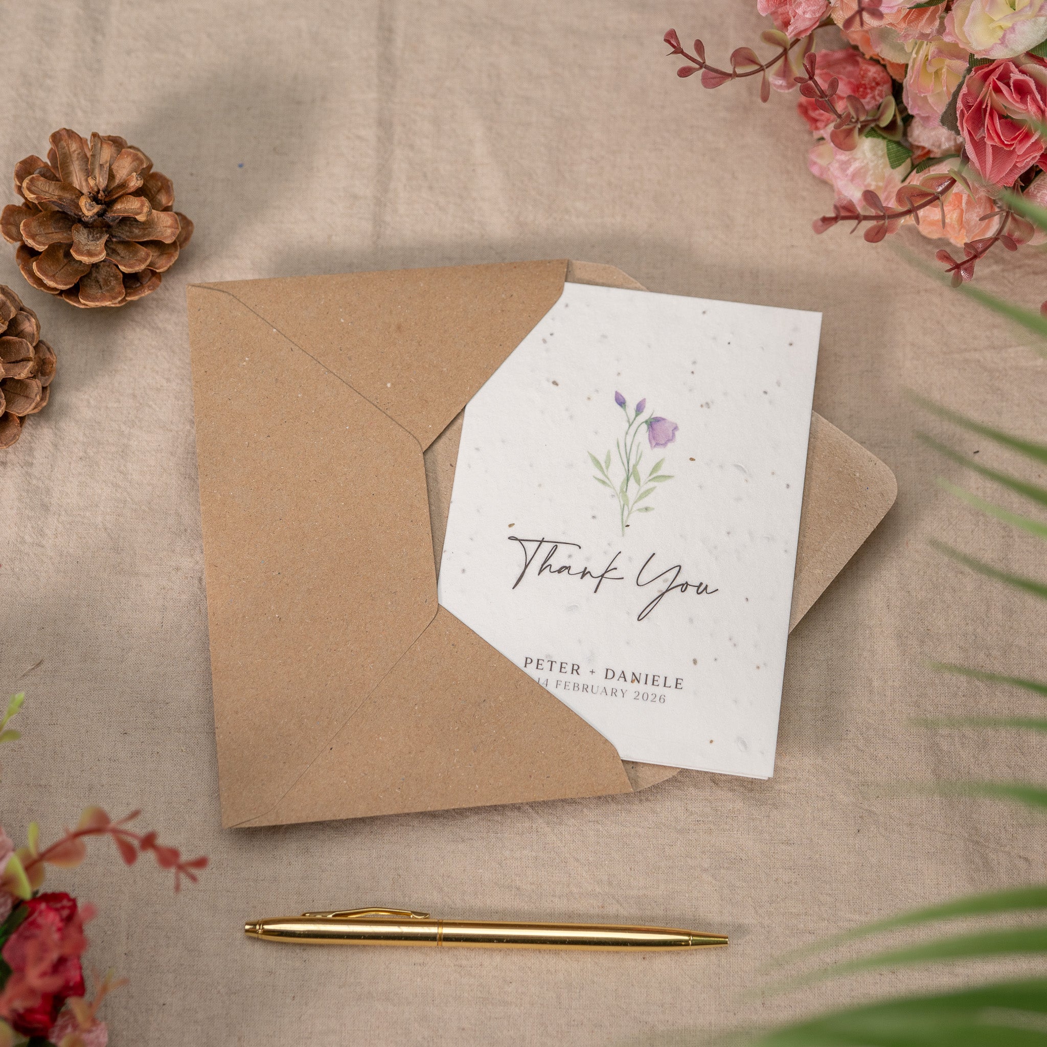 Brown envelope with a white card featuring floral designs and 'Thank You' text, on a beige surface with decorative elements.