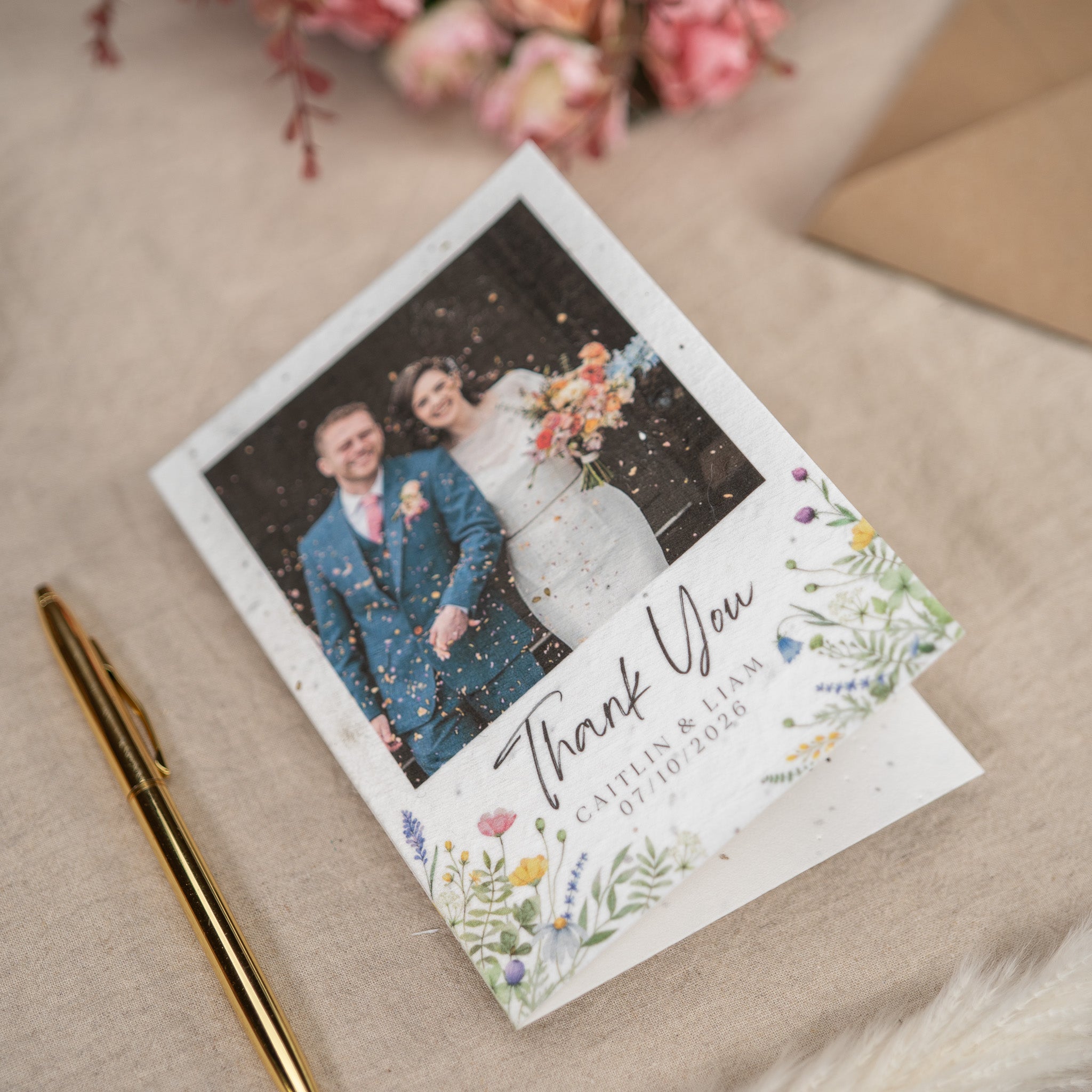 Wedding thank you card with couple photo and floral design on a beige surface.