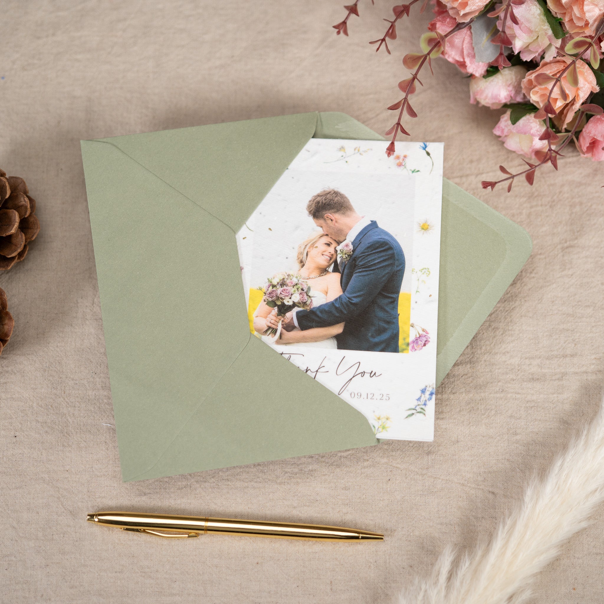 Floral wedding greetings card inside a green envelop on a textured surface surrounded by a gold pen and flowers