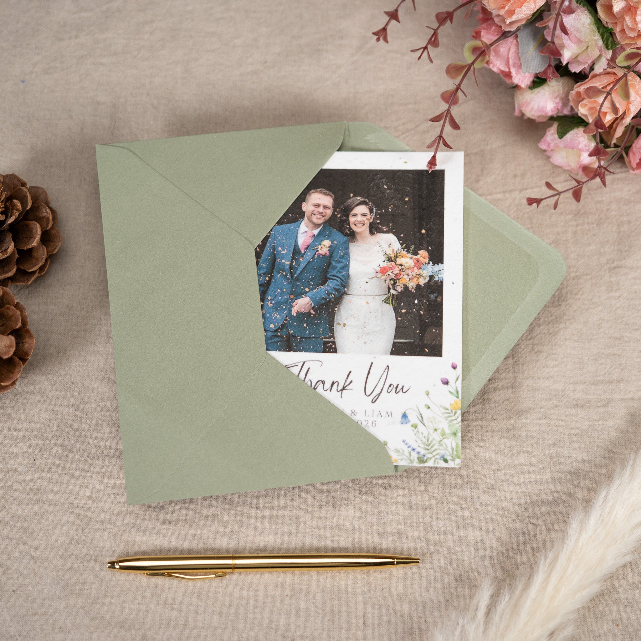 Wedding thank you card with a photo of a couple on a green envelope, surrounded by flowers and a pen.