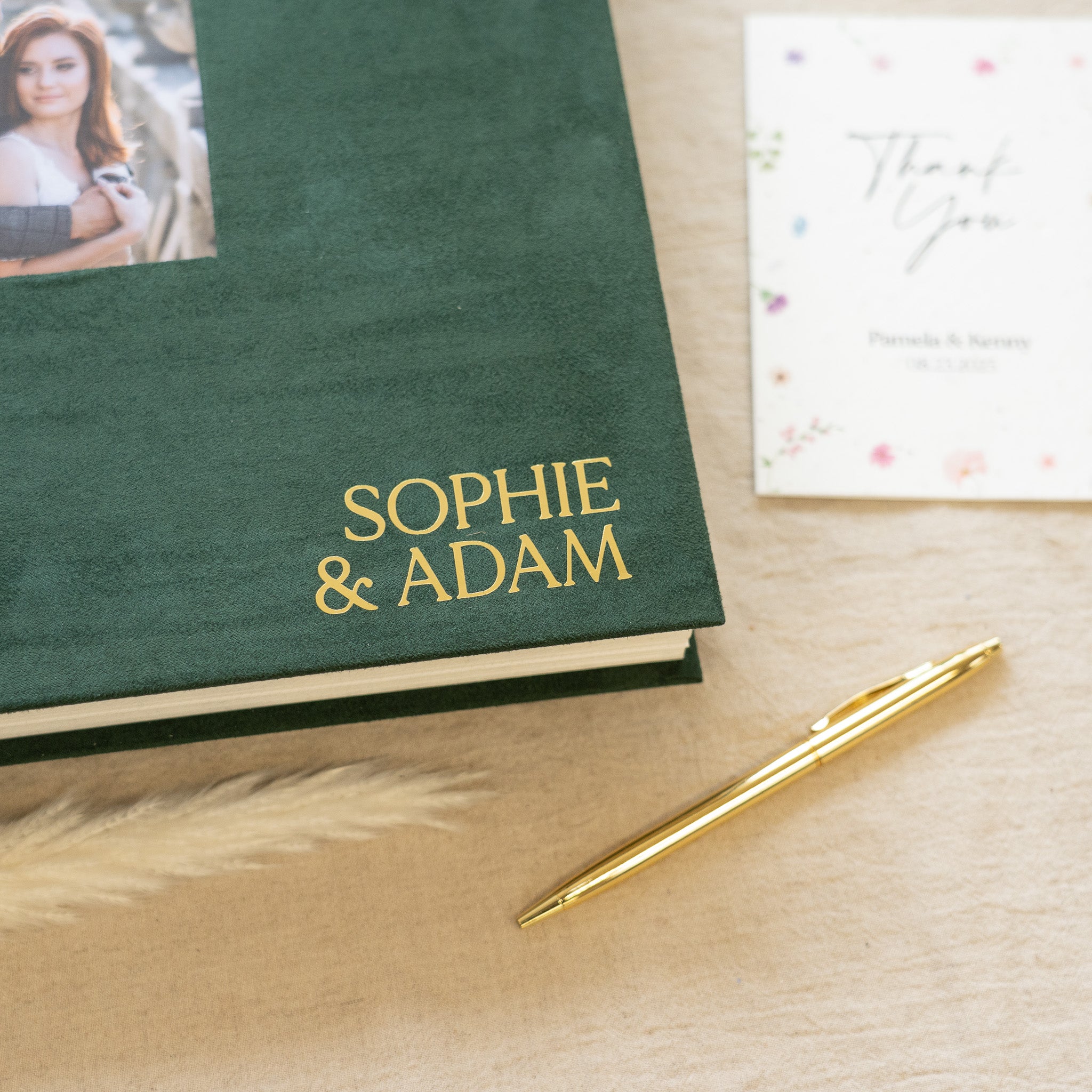 Green book with 'Sophie & Adam' on a wooden surface with a gold pen.