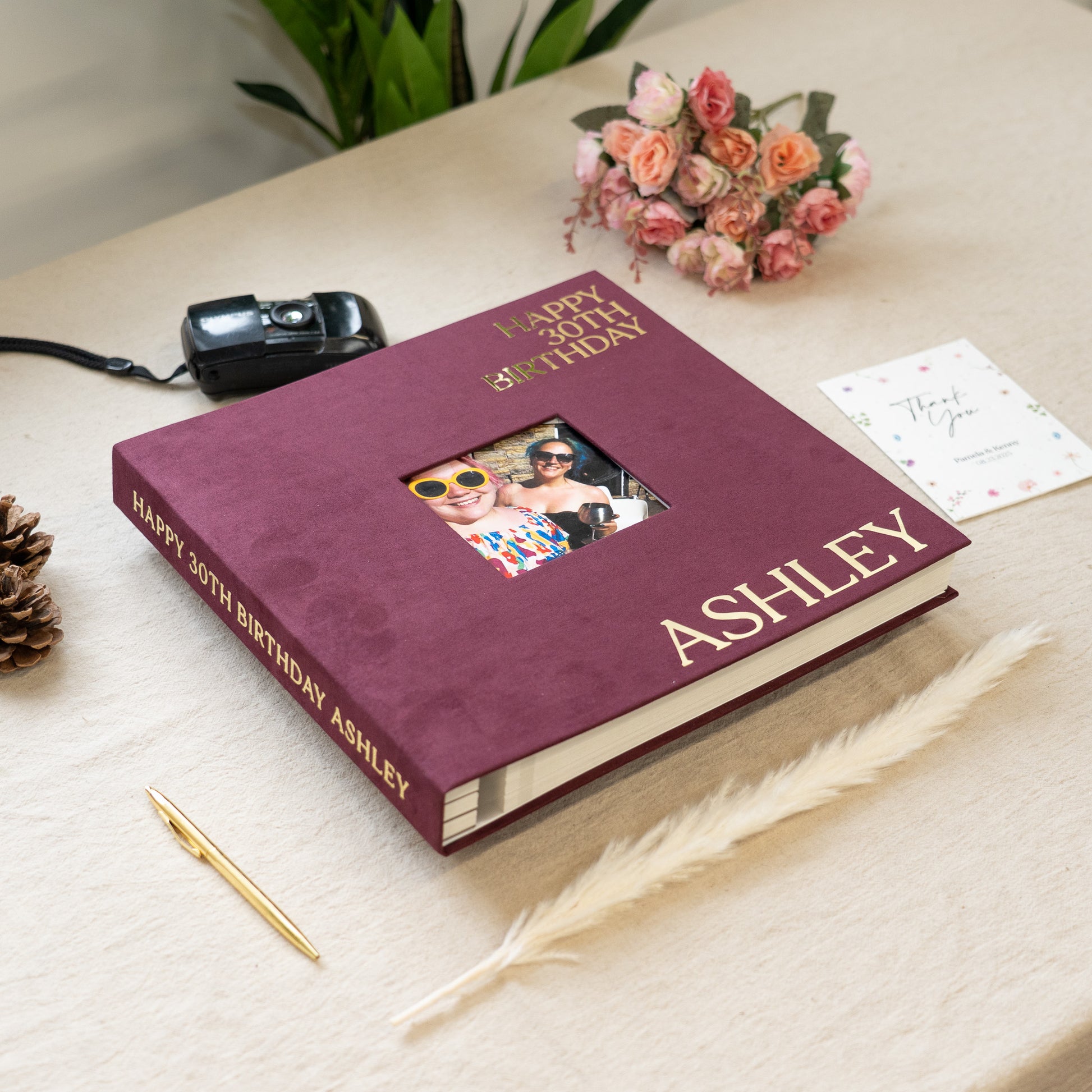 Personalized birthday album with photos on a table with a camera and flowers