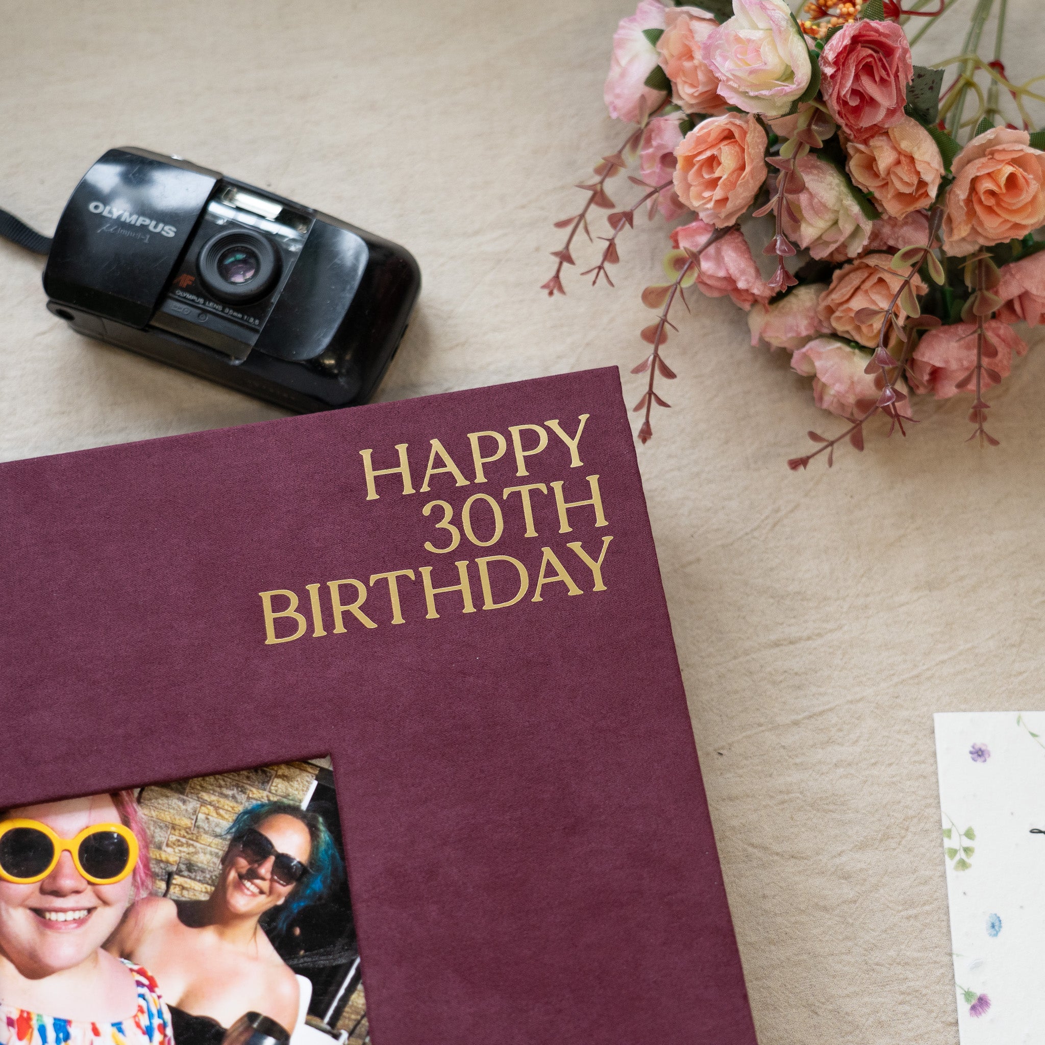 Maroon card with 'Happy 30th Birthday' text, camera, and flowers on a wooden surface