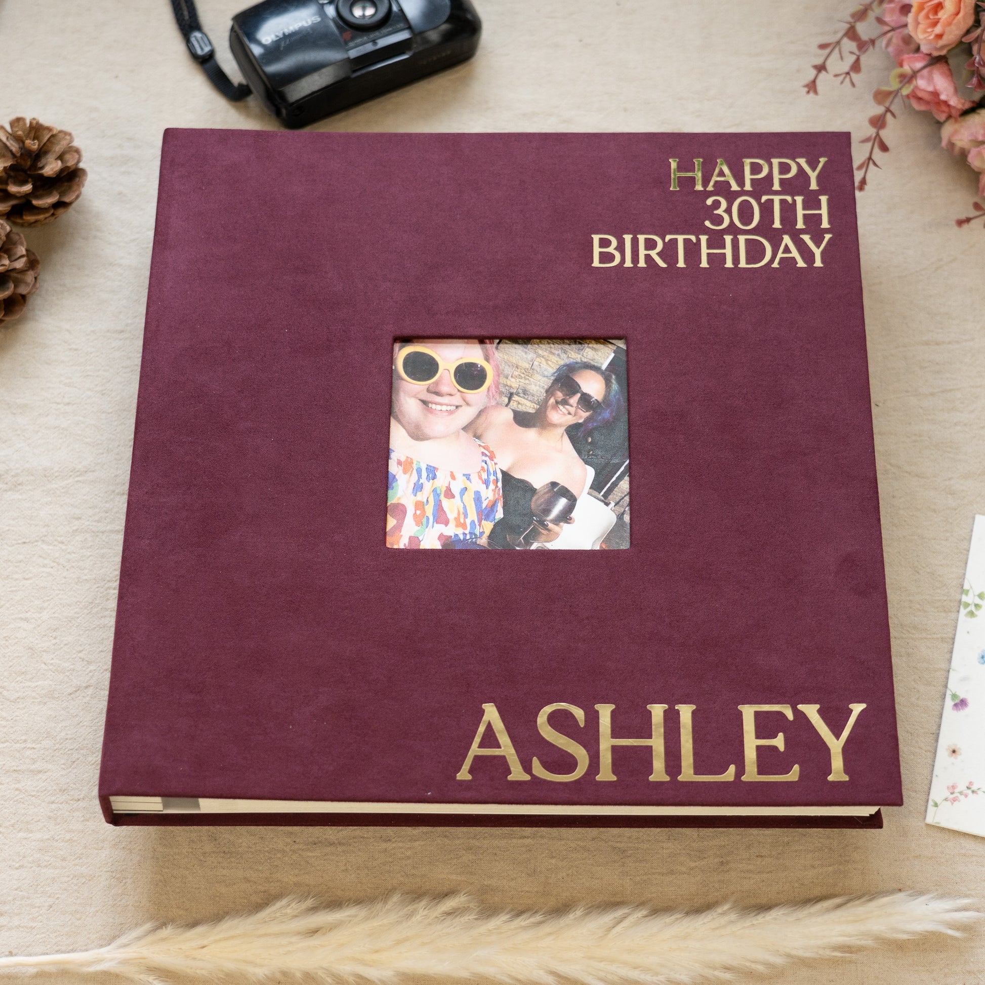 Personalized birthday album with a photo of two people and the text 'Happy 30th Birthday Ashley' on a wooden surface.