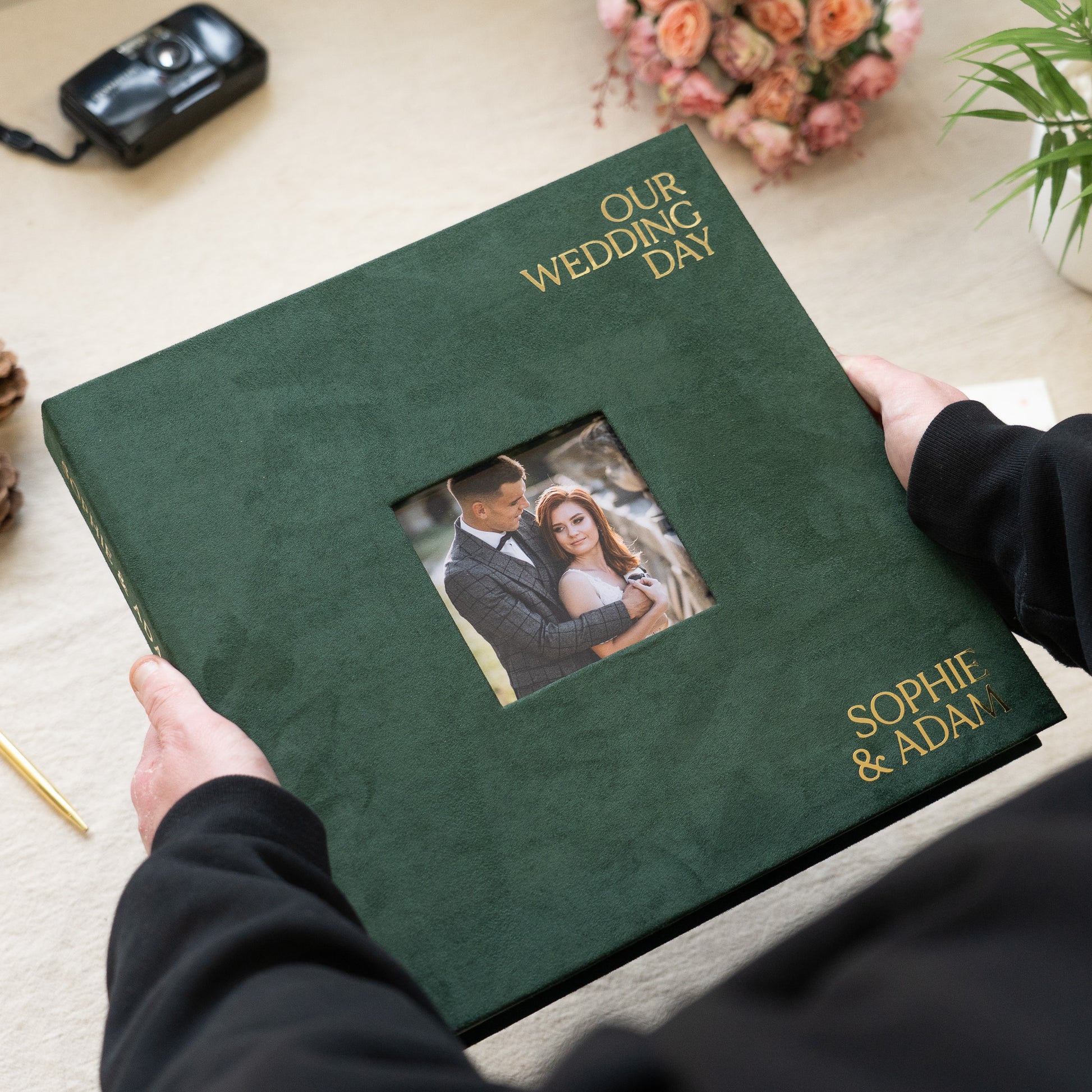 Green wedding album with a photo of a couple and text 'Our Wedding Day' held by a person.