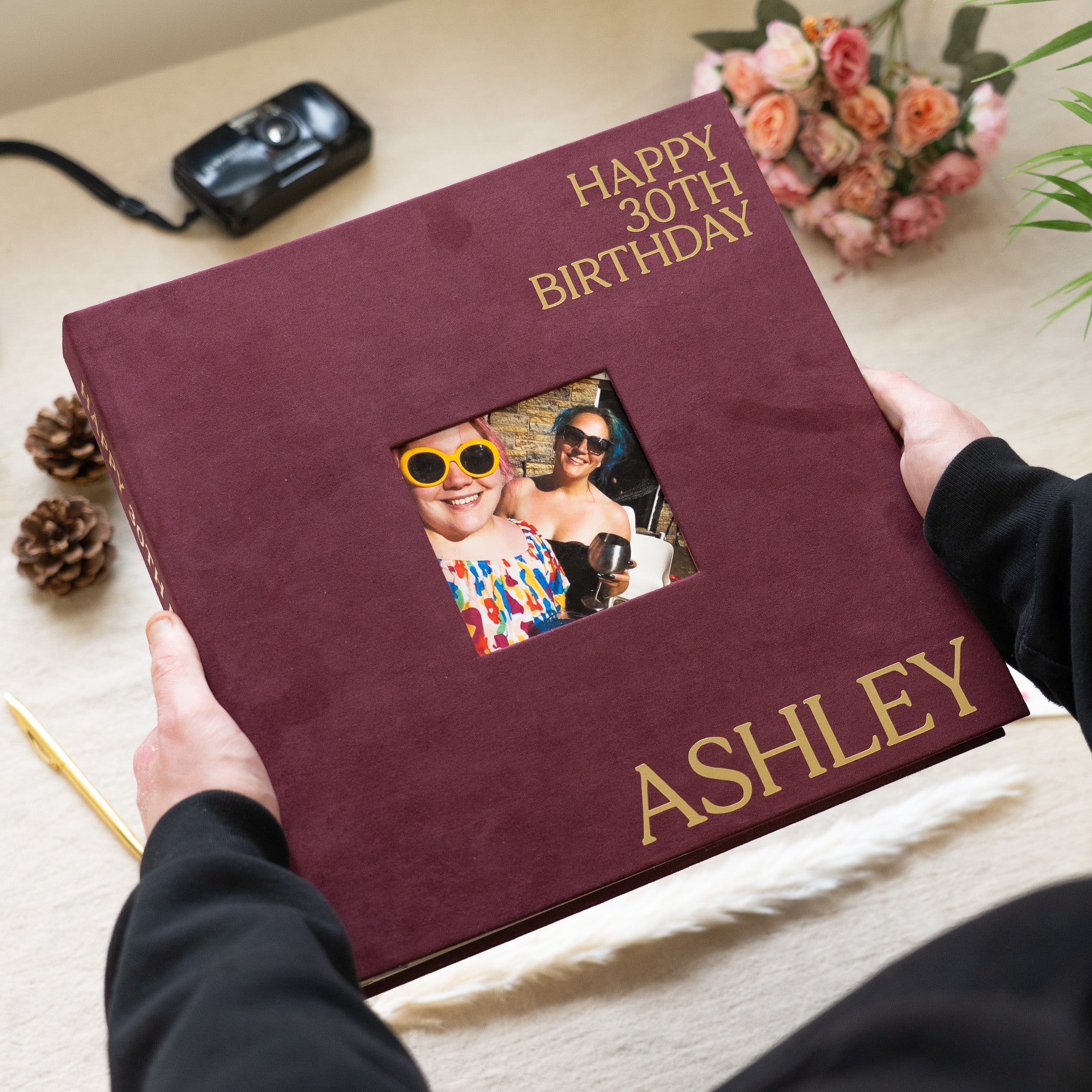 Maroon birthday album with gold text and a photo of two people on a light surface.