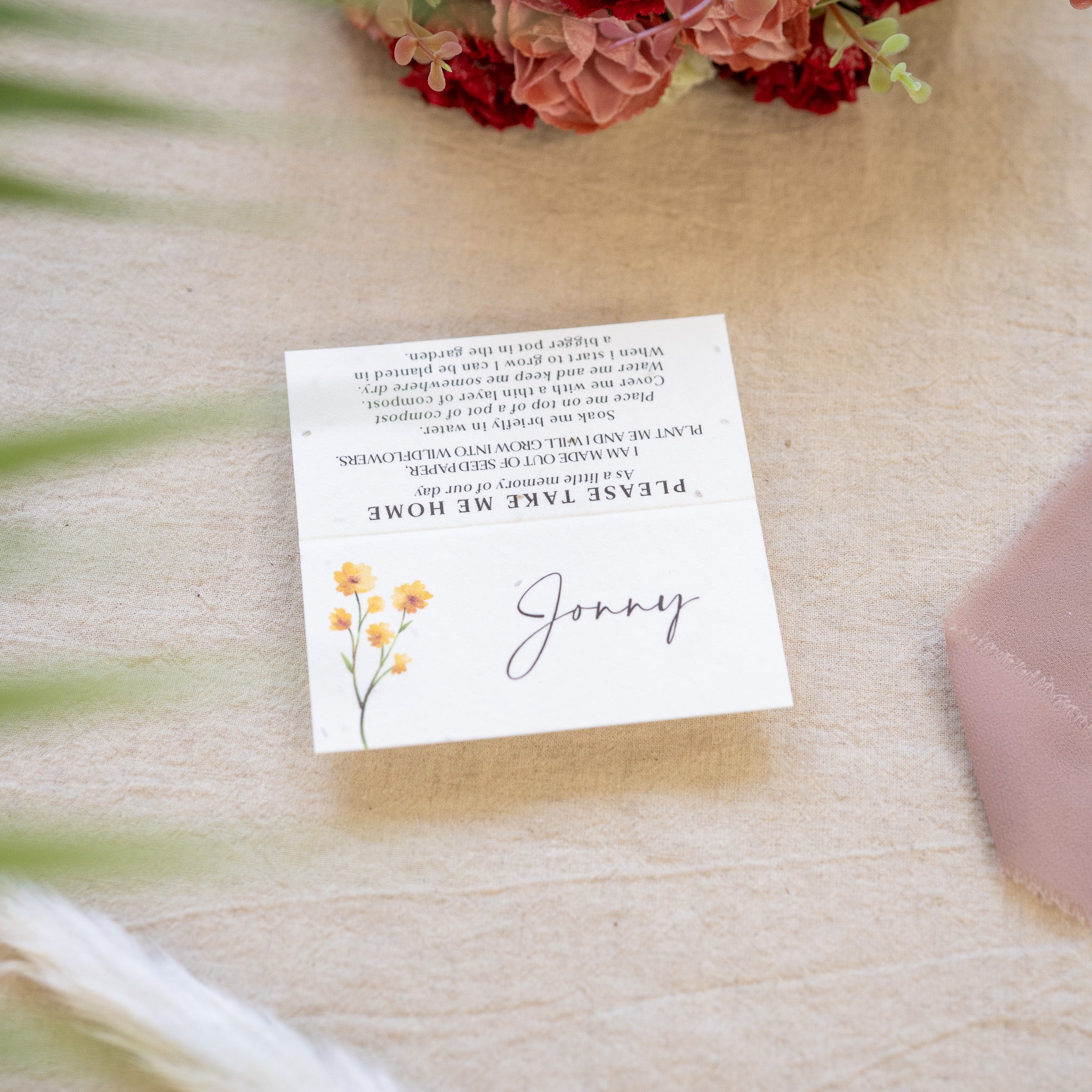 White card with text and floral design on a textured surface with flowers in the background
