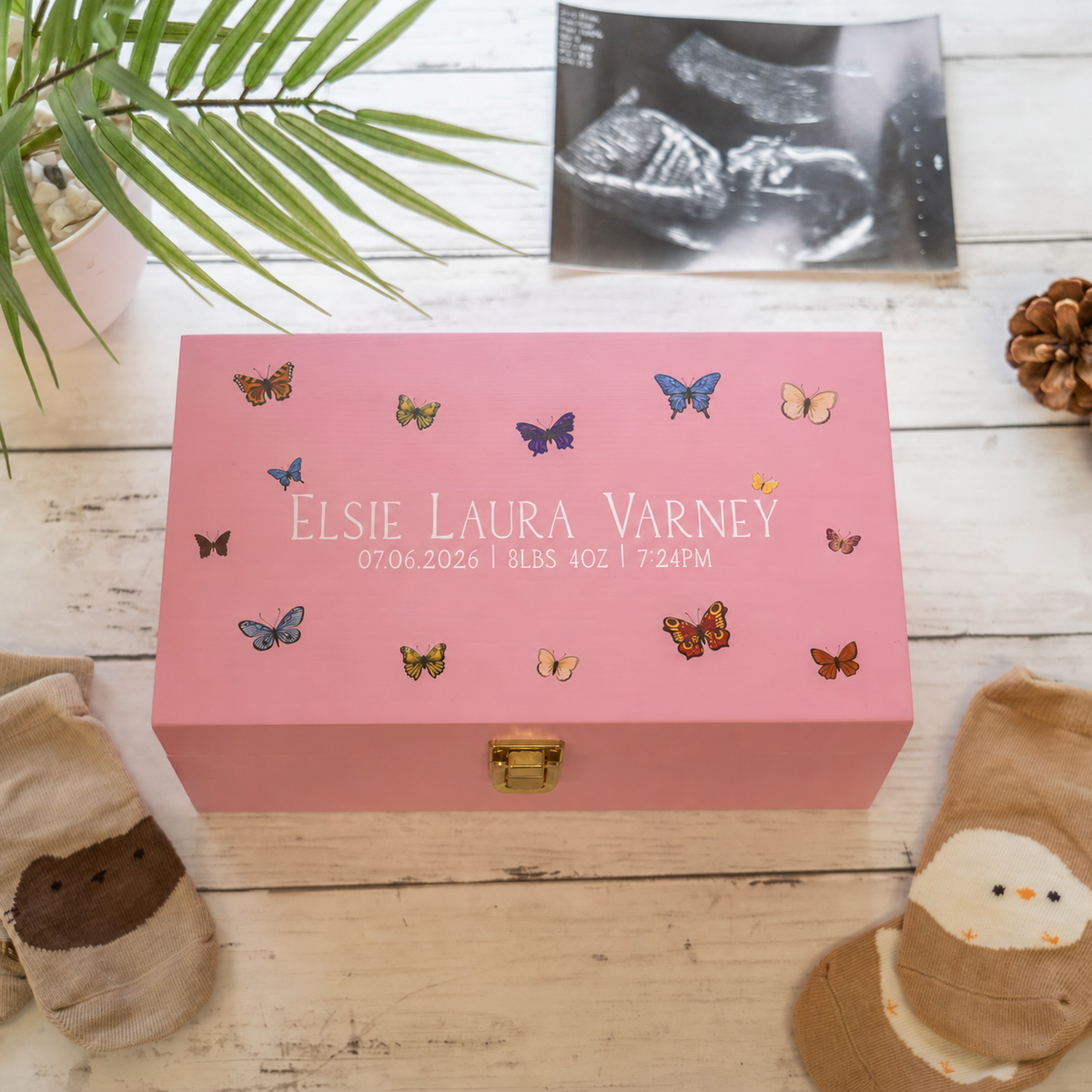 A pink personalized keepsake box with a gold clasp, decorated with colorful butterfly illustrations and the text 'Elsie Laura Varney 07.06.