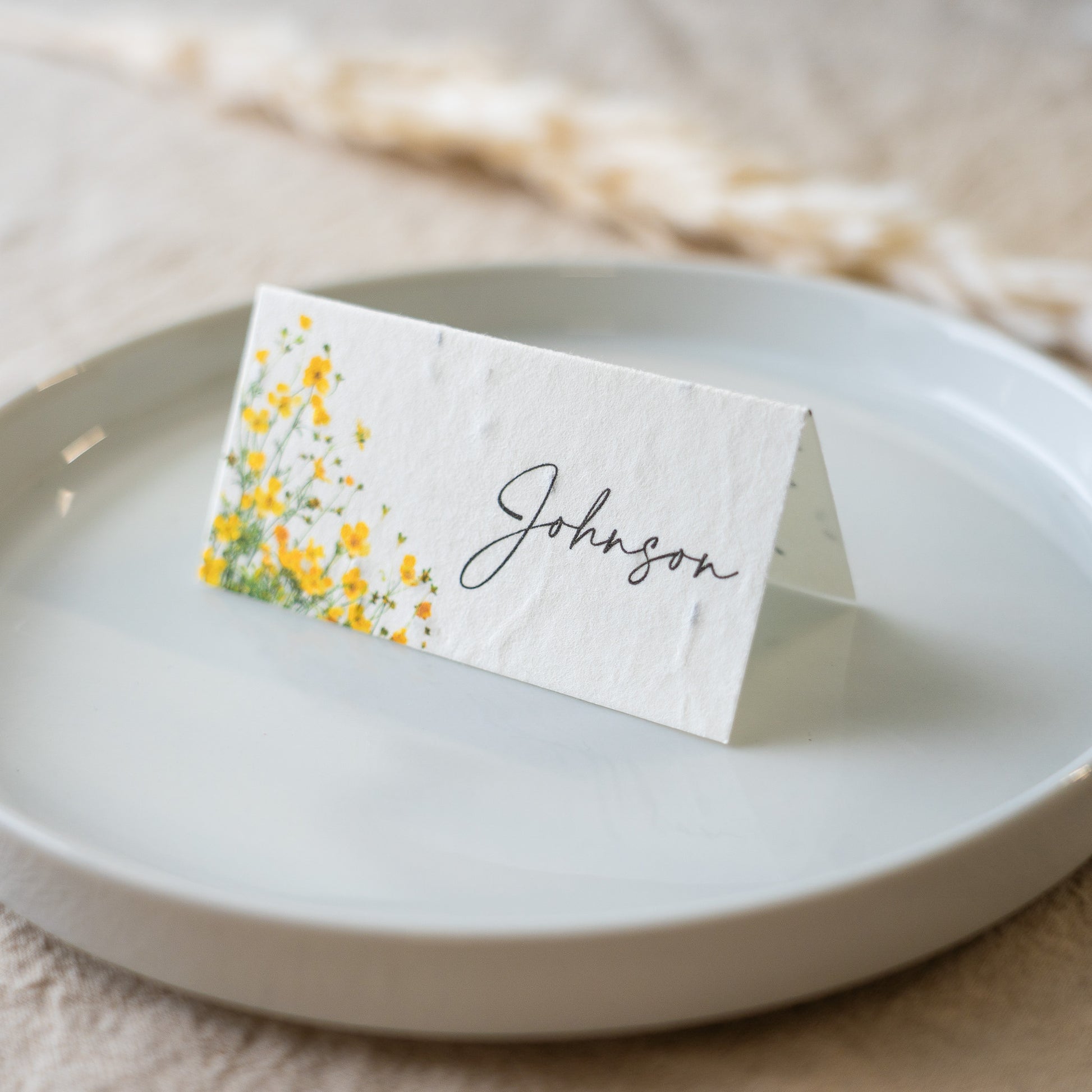 Place card with yellow floral design and 'Johnson' text on a white plate.