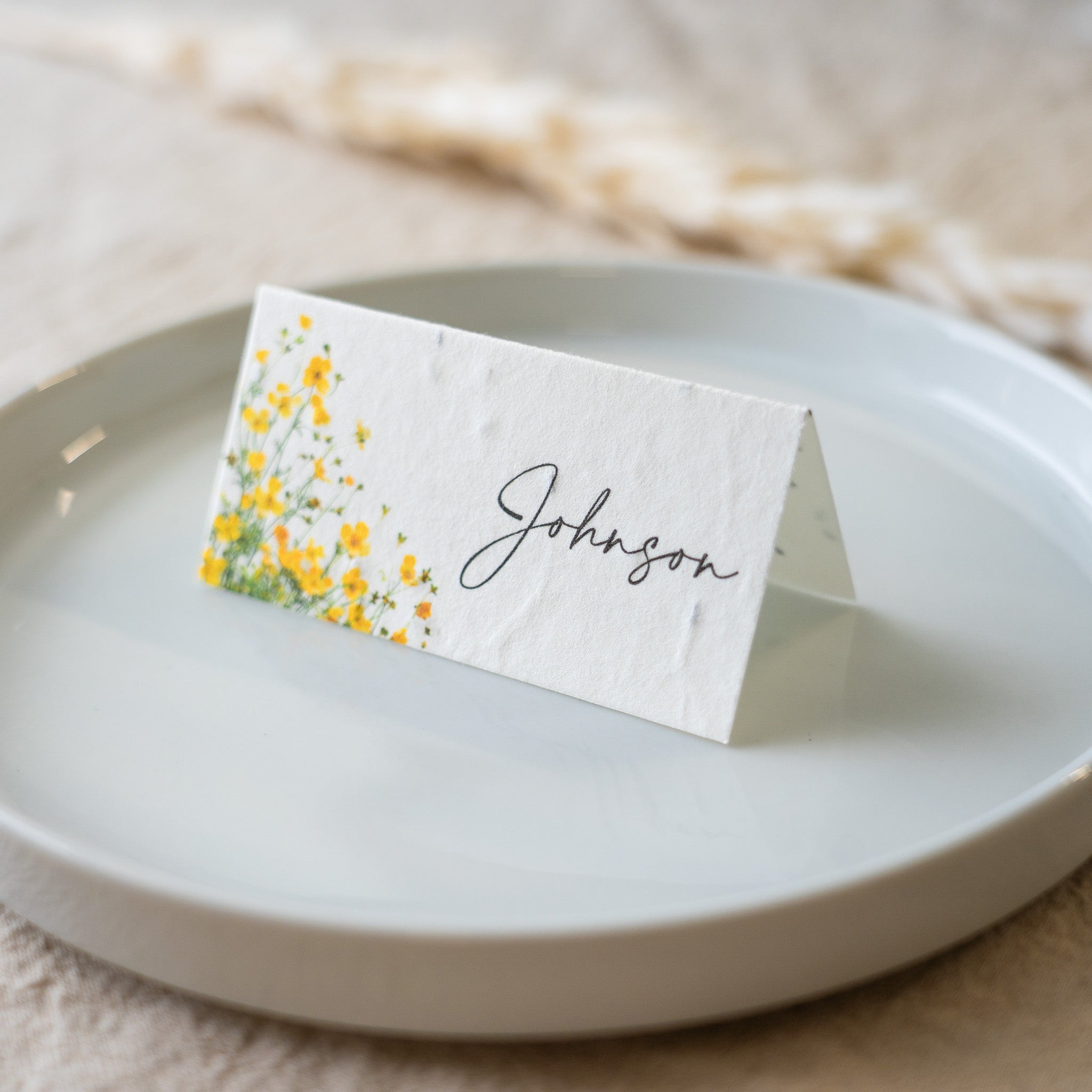 Place card with yellow floral design and 'Johnson' text on a white plate.