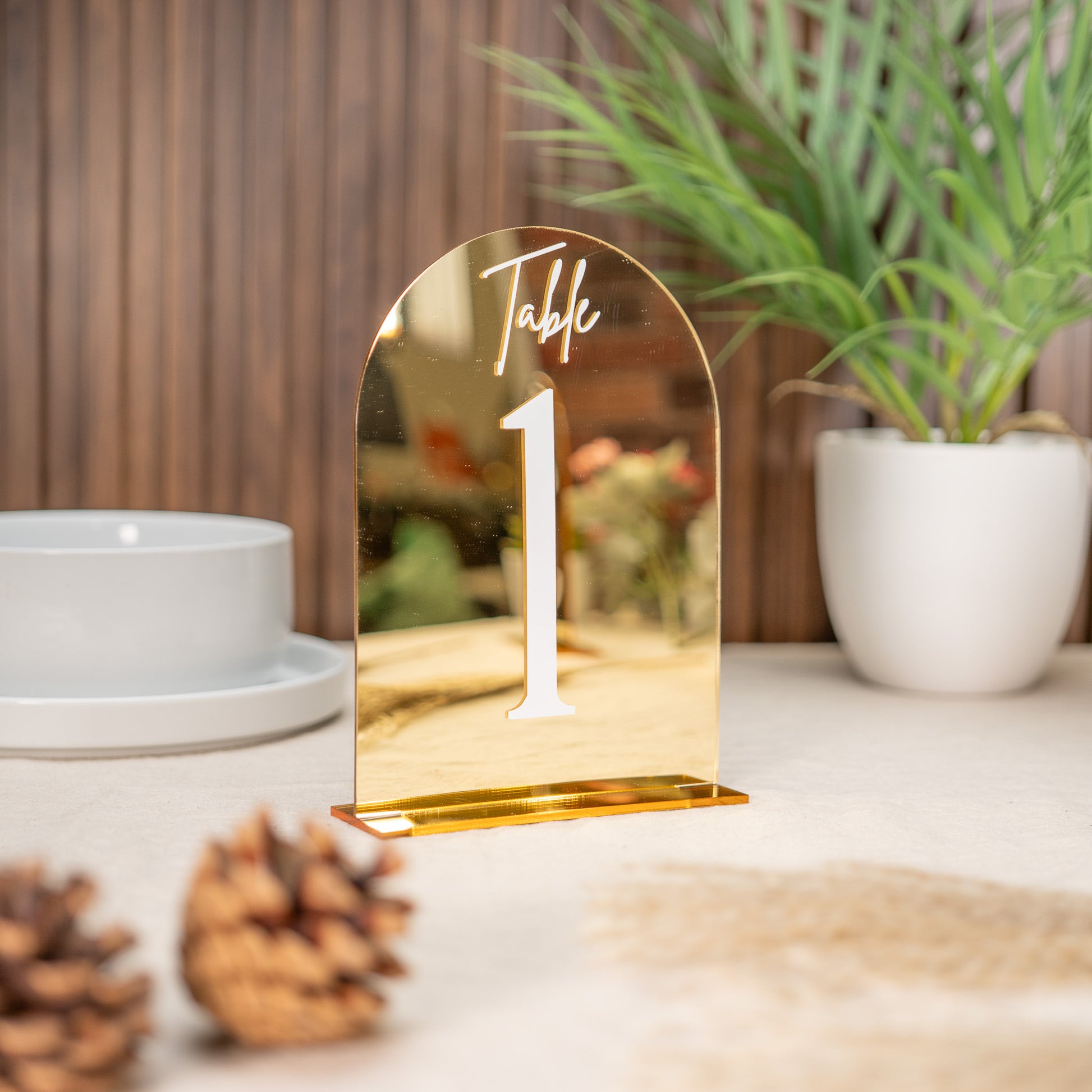 Gold table number on a surface with decorative elements and plants in the background