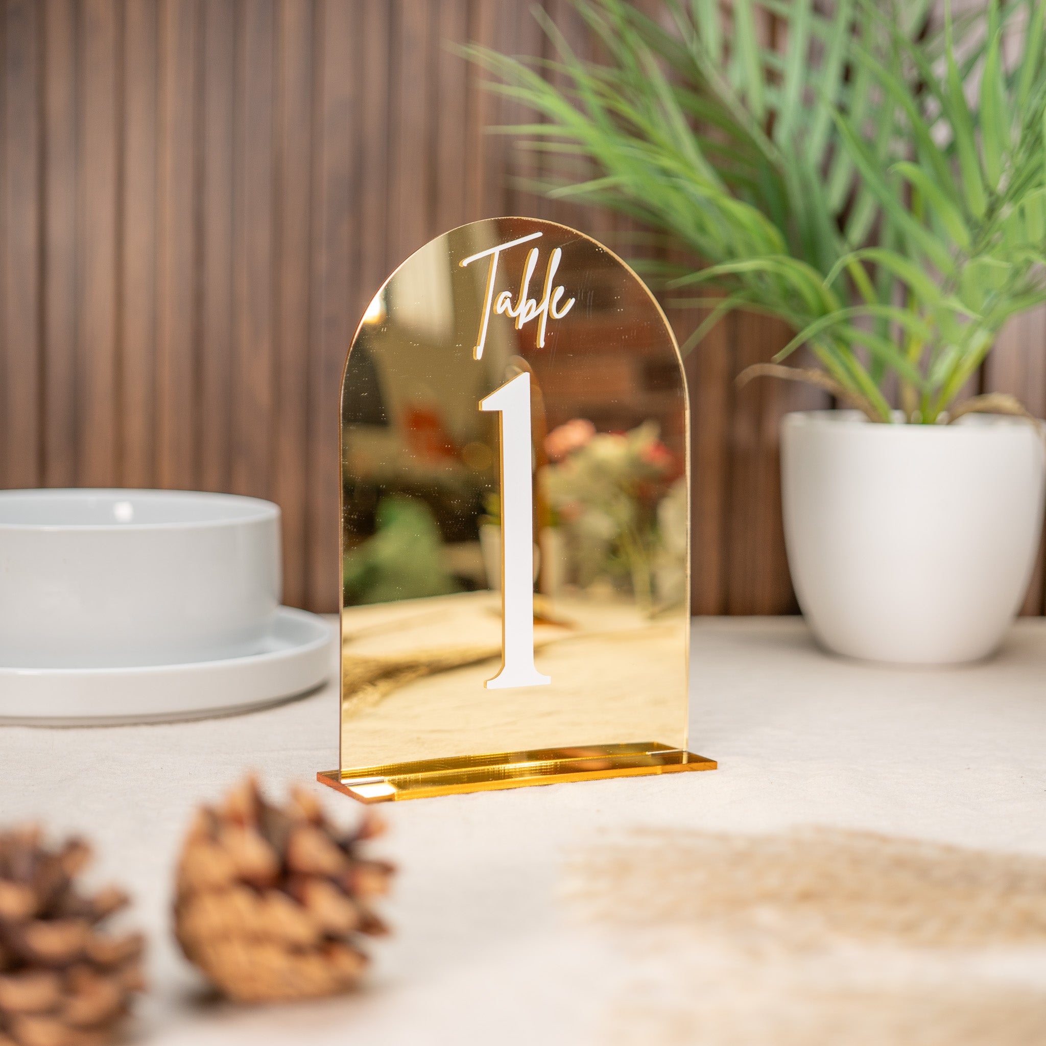 Gold table number on a surface with decorative elements and plants in the background