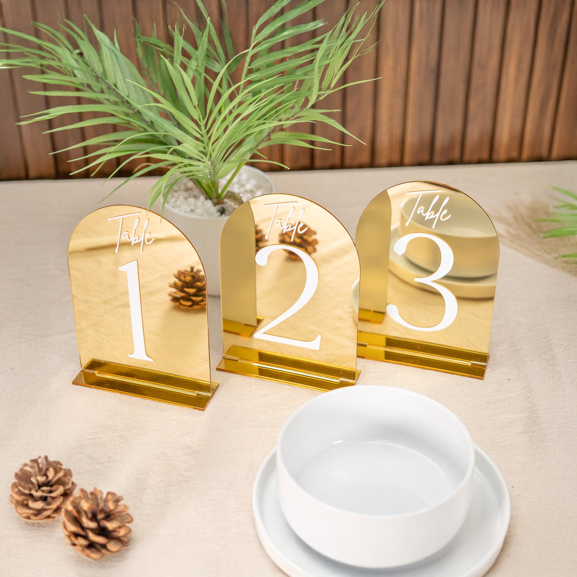 Gold table number holders with numbers 1, 2, and 3 on a table setting with a plant and decorative items.