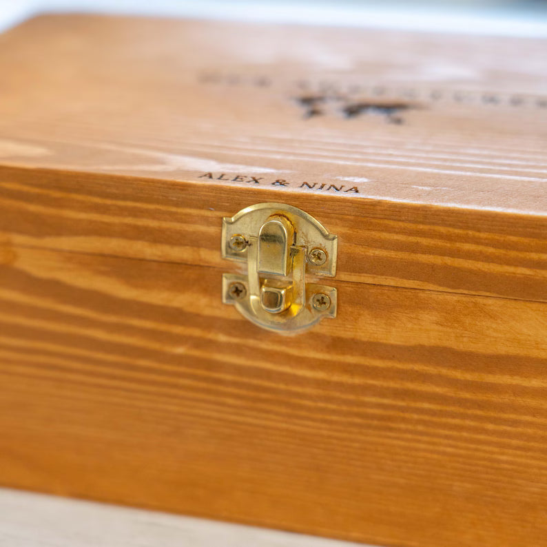 Close-up of a wooden presentation box lid with a brass clasp and engraved text reading 'ALEX & NINA'.