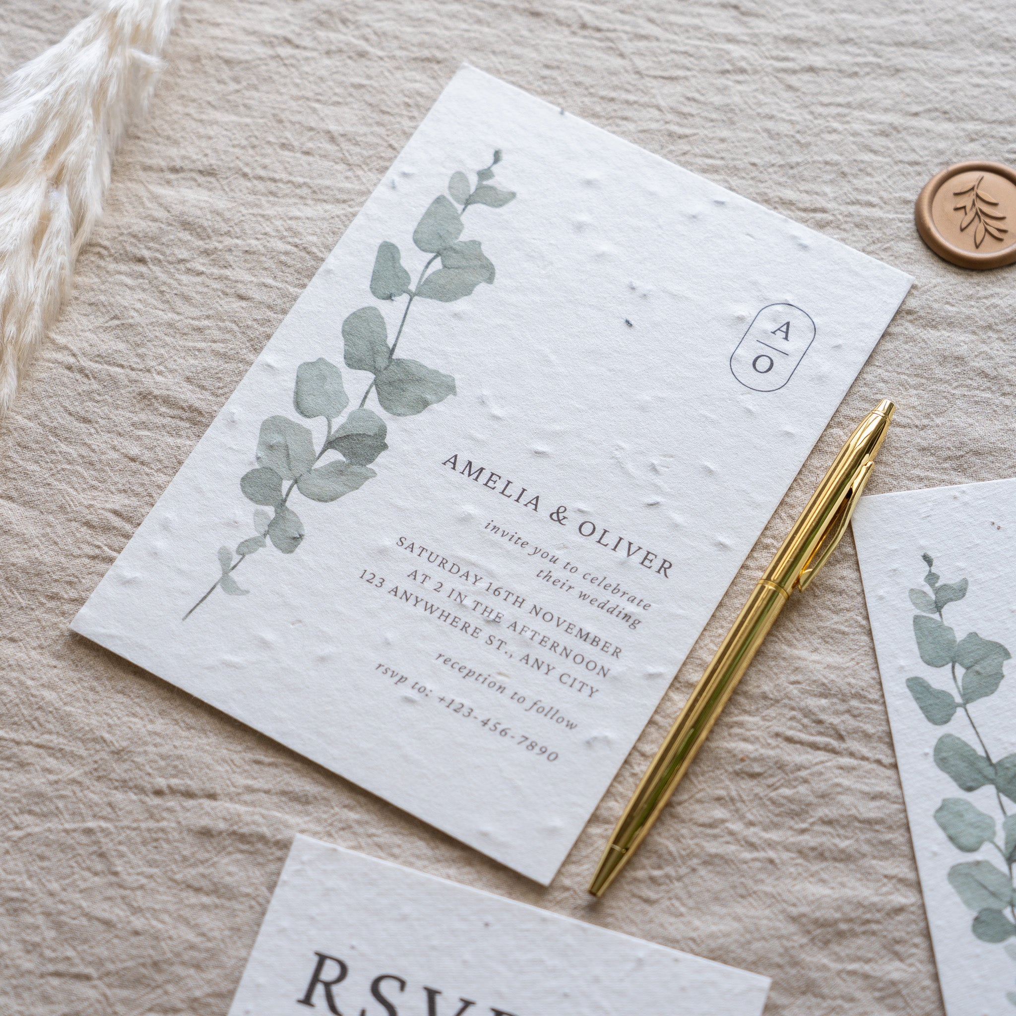 Wedding invitation with eucalyptus design on a textured surface with a pen and RSVP card.