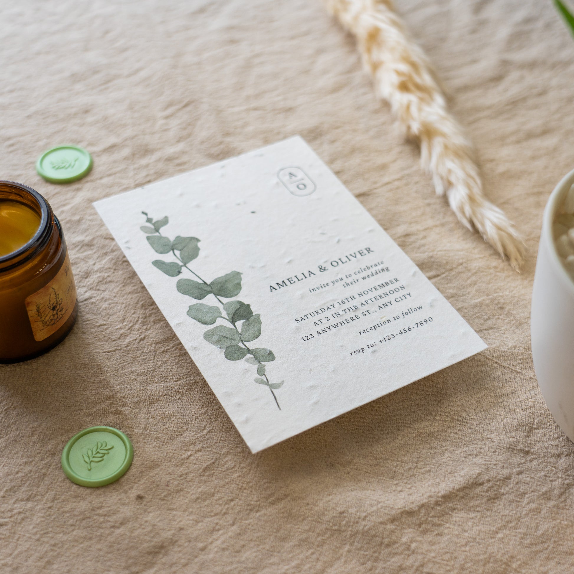 Invitation card with eucalyptus design on a textured surface with a candle and decorative elements.