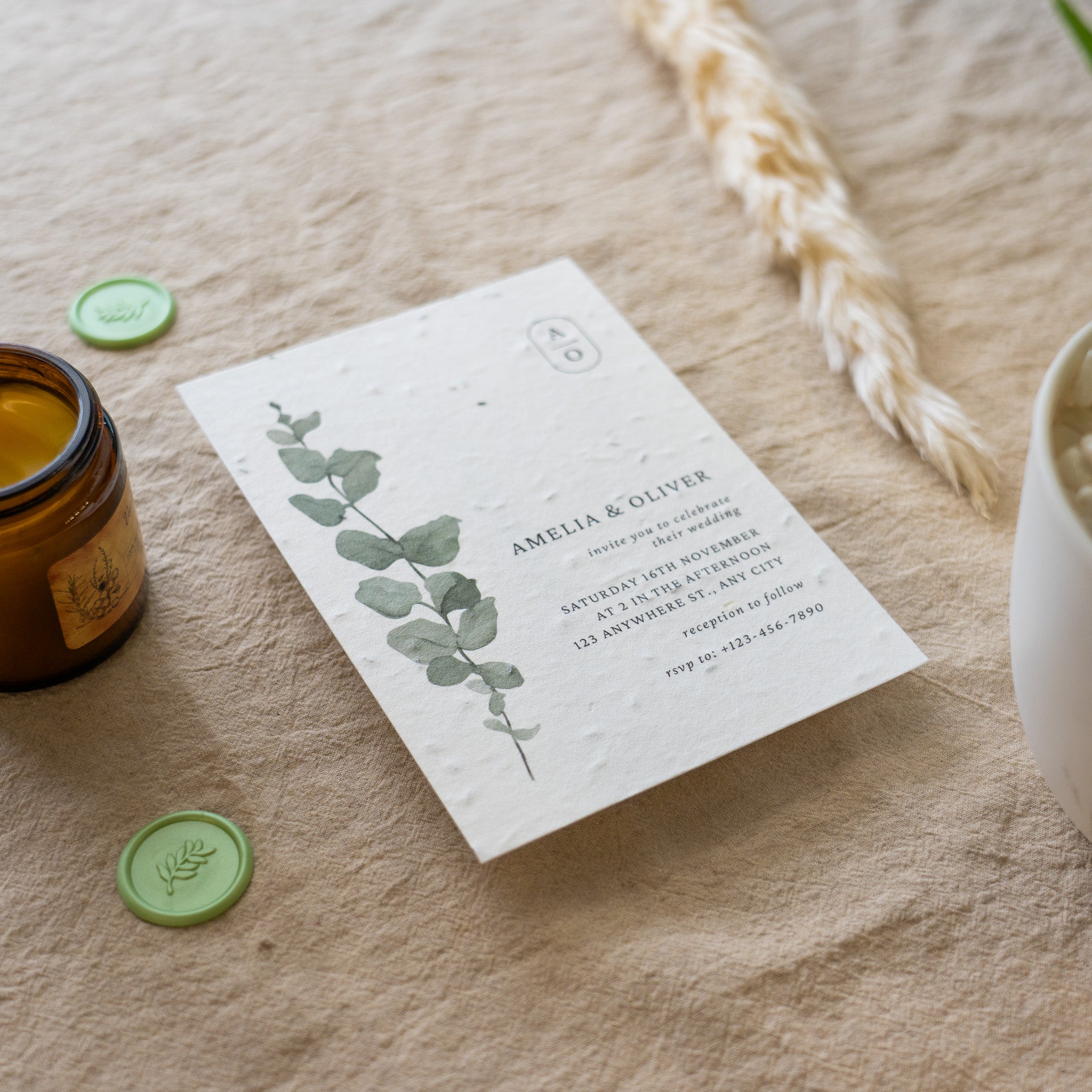 Invitation card with eucalyptus design on a textured surface with a candle and decorative elements.