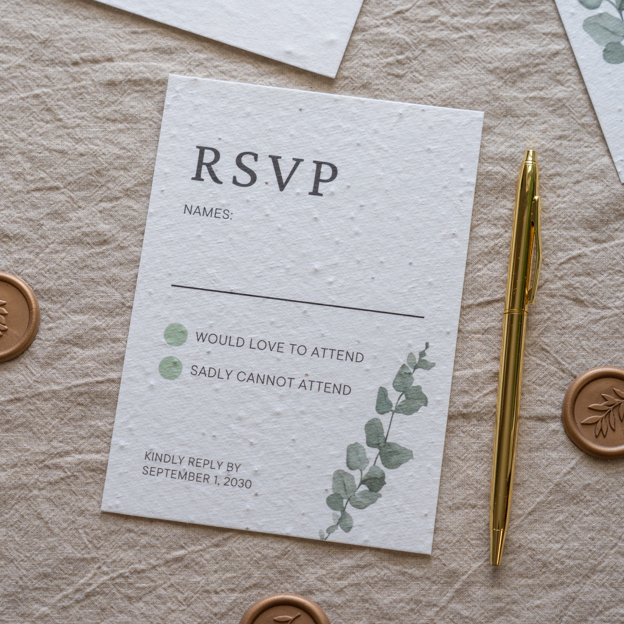 RSVP card with greenery design on a textured surface with a pen and seals.