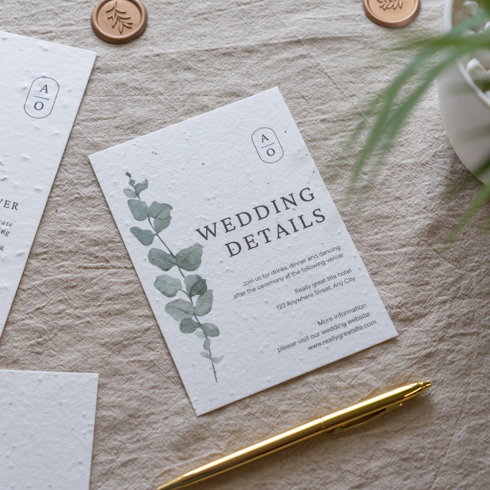 Wedding details card with eucalyptus design on textured surface with gold pen